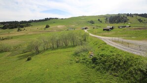 A rural landscape with rolling hills, a dirt road, and several small buildings. - South Apartment, 8 pers, 44m², panoramic slopes (Les Saisies)