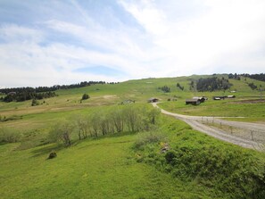 A rural landscape with rolling hills, a dirt road, and several small buildings.