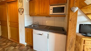 A compact kitchen with wooden cabinets, a microwave, a dishwasher, and a small wooden table with a television. - South Apartment, 8 pers, 44m², panoramic slopes (Les Saisies)