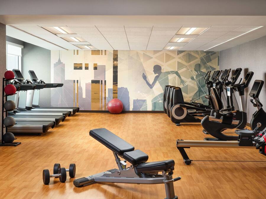 Ein Fitnessstudio mit Laufbändern, Crosstrainern, einer Bank und Kurzhanteln.