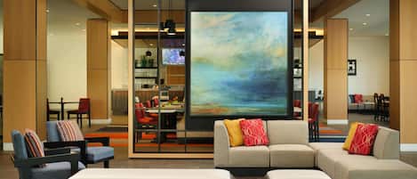 Een moderne hotel lobby met een groot abstract schilderij, comfortabele zitplaatsen en een bar.