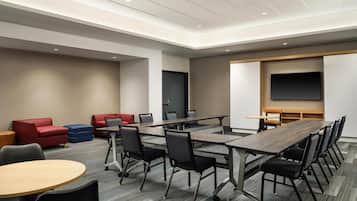 A conference room with a long table, chairs, a TV screen, and a red and blue sofa.