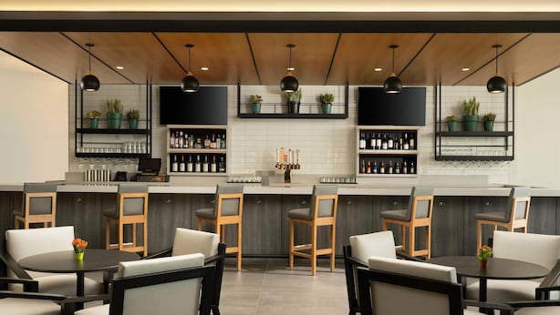 Un espace bar moderne, doté d’un long comptoir, de nombreux tabourets et d’étagères remplies de bouteilles et de verres.