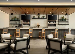Een moderne bar met een lange toonbank, verschillende barkrukken en planken vol flessen en glazen.