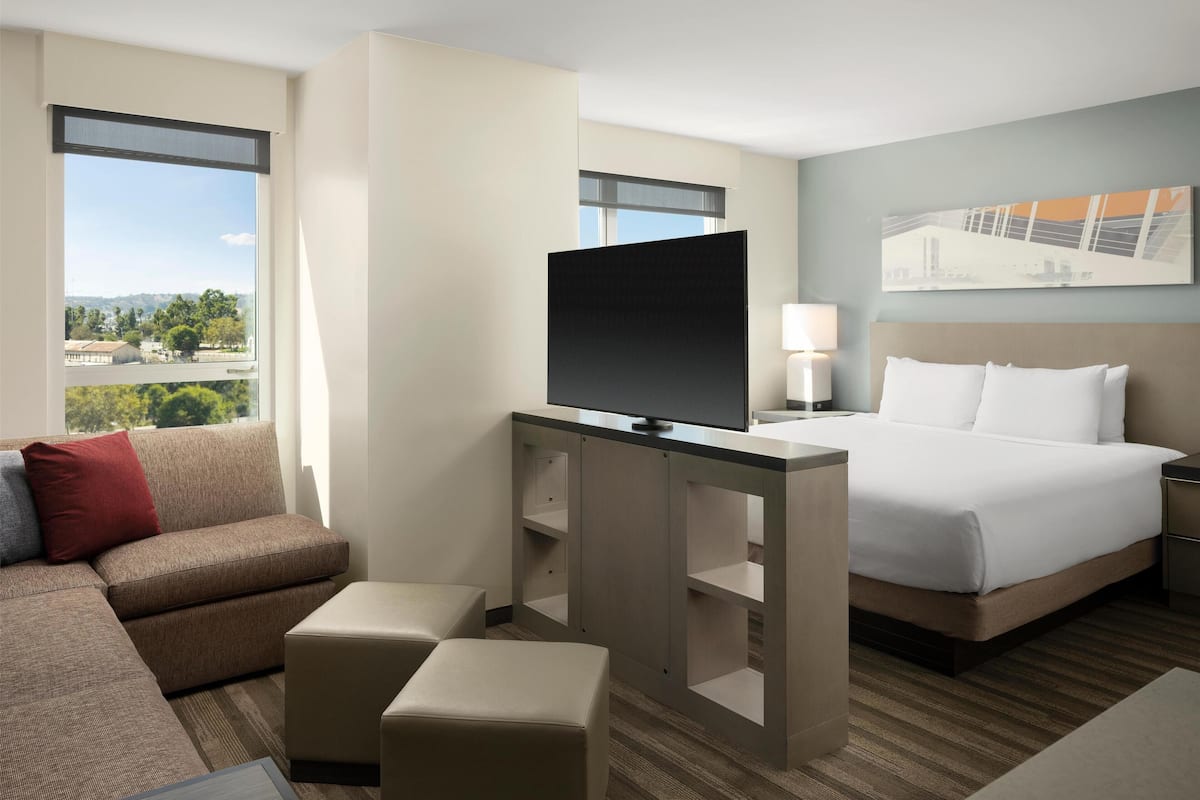 Une chambre d’hôtel avec un grand lit, un téléviseur posé sur un meuble, un canapé et une vue sur la ville.