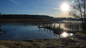 A serene lakeside scene with a wooden dock extending into the water, surrounded by trees and a clear sky. - Ferienhaus am See in Fleeth (Mirow)