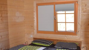 A wooden cabin bedroom with a bed, a window with blinds, and a wooden ceiling. - Ferienhaus am See in Fleeth (Mirow)