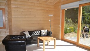 A log cabin interior with a leather sofa, a wooden coffee table, and a sliding glass door leading to an outdoor area. - Ferienhaus am See in Fleeth (Mirow)