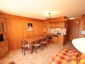 Een kleine keuken met houten kastjes, een eettafel met stoelen en een klein oven.