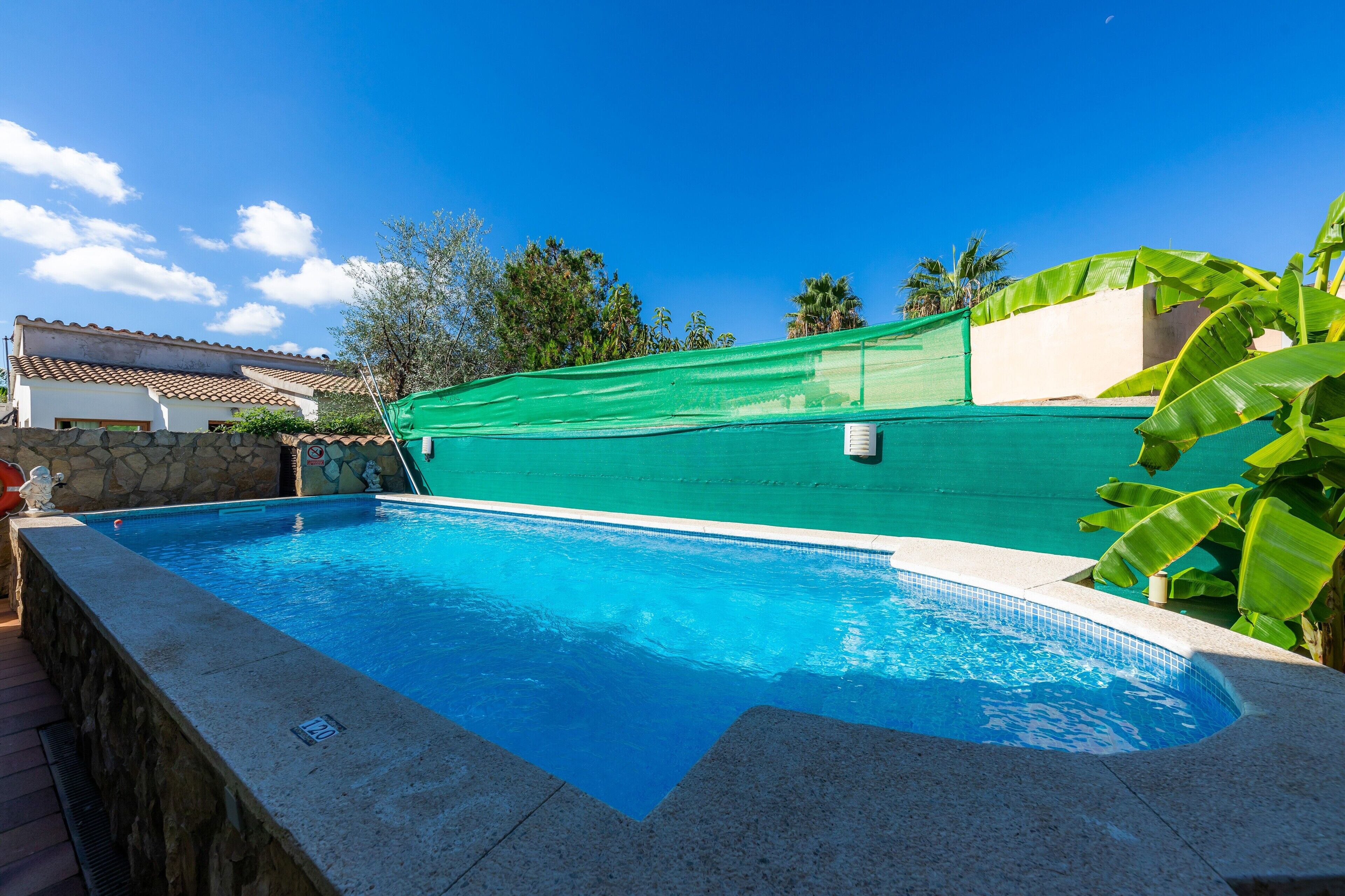 Una piscina con un muro de piedra, una red verde y un cielo azul despejado.
