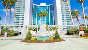 Un hotel moderno con fachada curva, un atrio central de cristal y palmeras en primer plano.