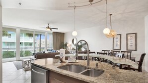 Una cocina moderna con encimera de granito, pileta de acero inoxidable y comedor con mesa de vidrio.