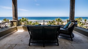 A balcony with two wicker chairs, a view of the ocean, and a railing with palm trees.