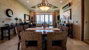 A dining area with a large round table, wicker chairs, and a chandelier.