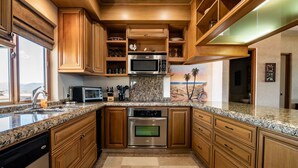 A modern kitchen with granite countertops, stainless steel appliances, wooden cabinets, and a view of the desert through a large window.