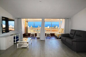 A living room with a sofa, a TV, a glass coffee table, and a balcony with a view of the sea. - Cozy townhouse with ocean views  (Costa Adeje)