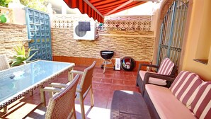 An outdoor patio with a glass table, wicker chairs, a sofa, and a barbecue grill.