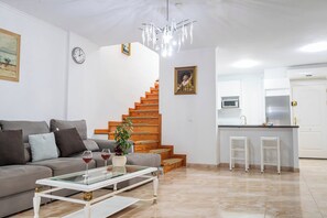 A modern living room with a sofa, coffee table, and a staircase leading to a kitchen area. - Cozy townhouse with ocean views  (Costa Adeje)