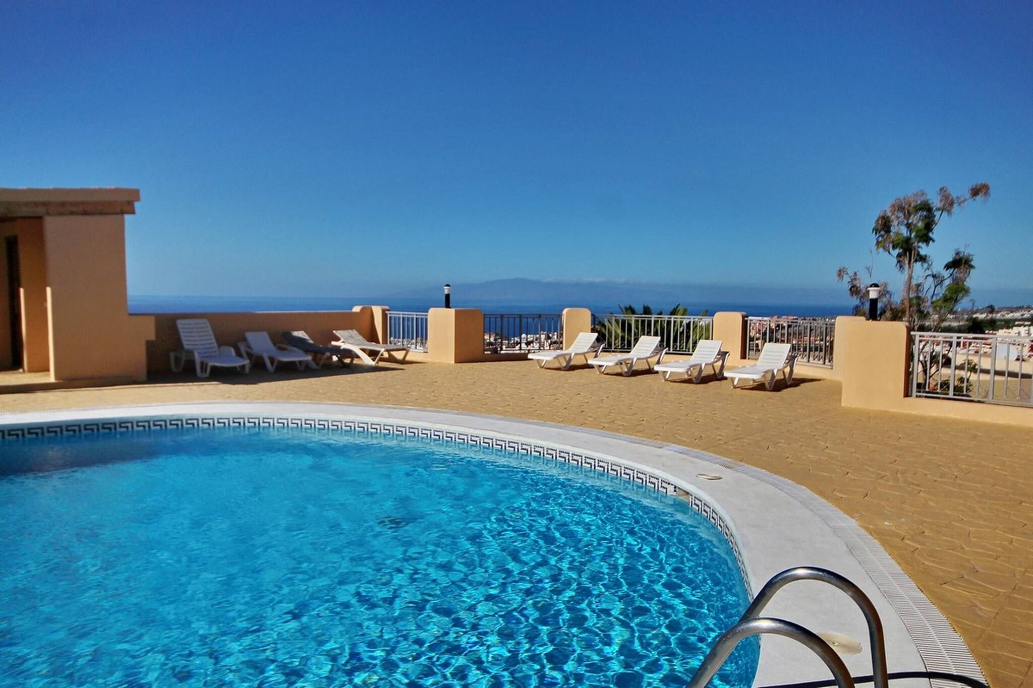 A pool with clear blue water, surrounded by lounge chairs and a view of the sea.