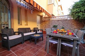 An outdoor patio with wicker furniture, a table set with fruit and drinks, and a decorative wall. - Cozy townhouse with ocean views  (Costa Adeje)