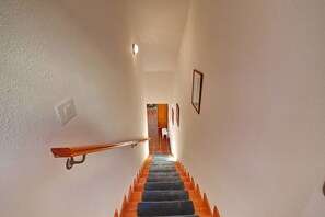 A staircase with a wooden handrail and a blue carpet leading to a room with a white door and a small white chair. - Cozy townhouse with ocean views  (Costa Adeje)
