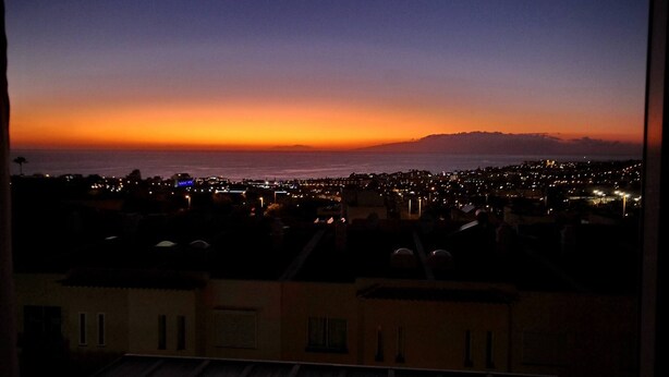 A cityscape at dusk with a view of the ocean and distant hills.
