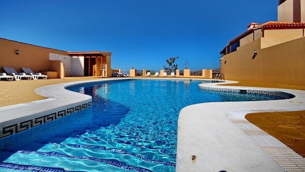 Una piscina amb aigua cristal·lina blava, envoltada d'una paret beix i una cantonada amb rajoles blanques.
