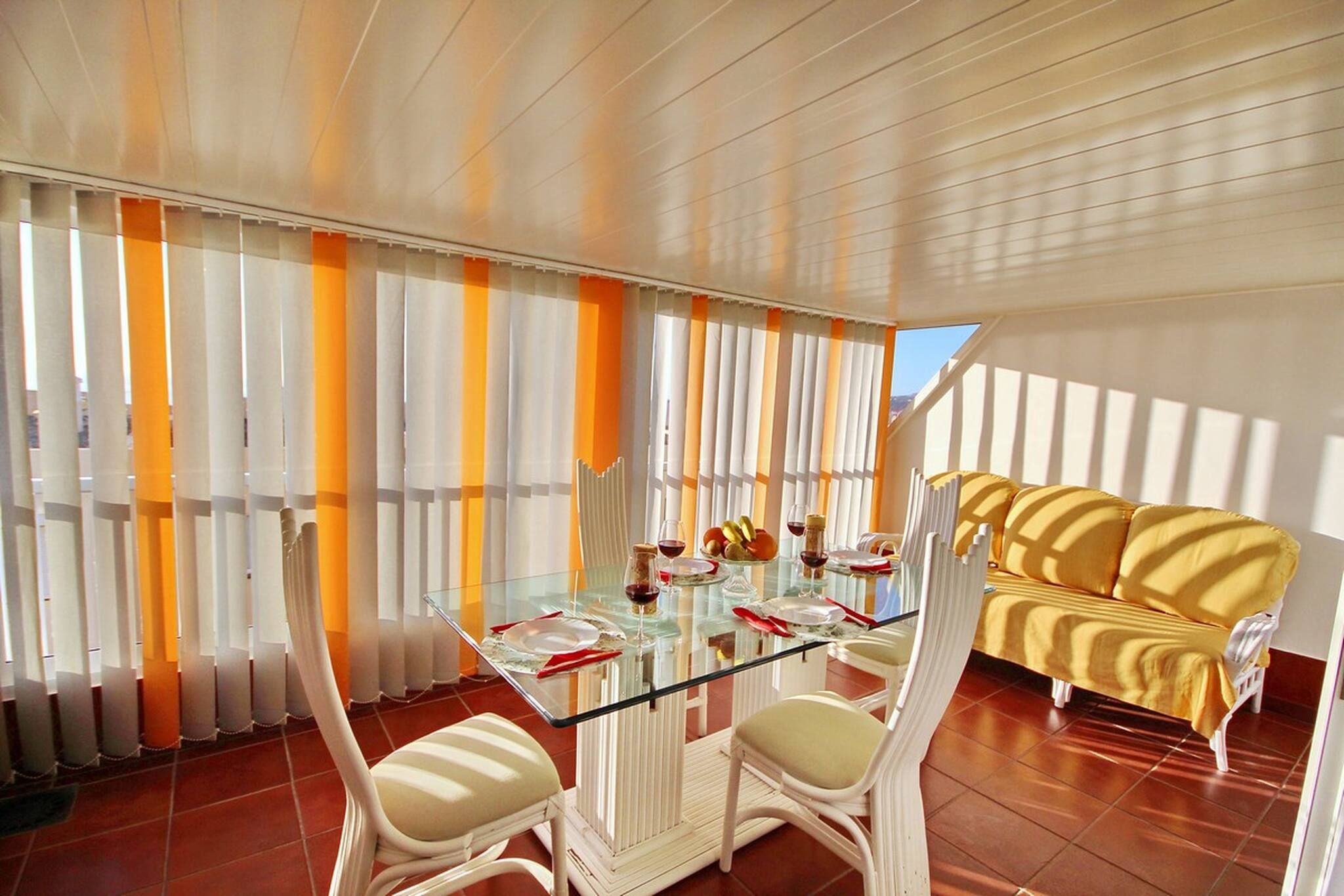 Un coin repas avec une table en verre, des chaises blanches et un canapé jaune.