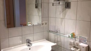 Ein Badezimmer mit einem weißen Waschbecken, einem Spiegel und einer Glasablage für Toilettenartikel.