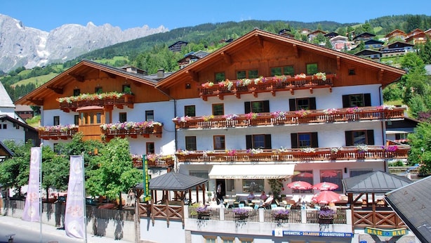 Ein traditionelles Holzhaus mit Balkonen, die mit Blumen geschmückt sind, einem Café und einer Bergkulisse.