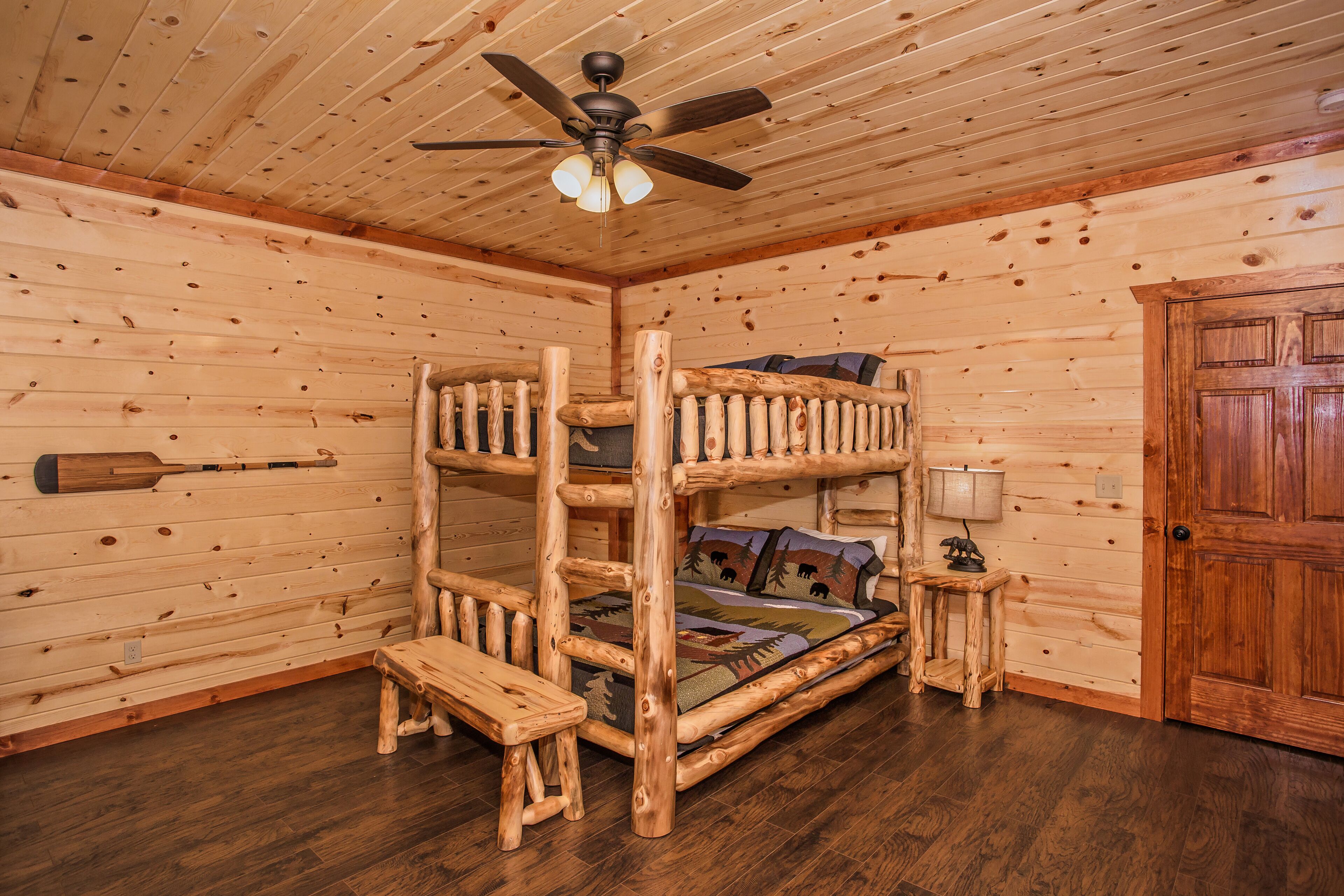 A cabin with a bunk bed, wooden walls, a ceiling fan, and a wooden door.