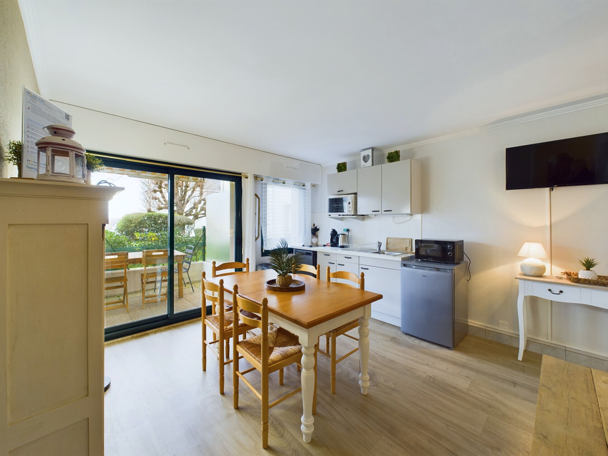 A modern kitchen with a dining area, a TV, and a sliding glass door leading to a balcony.