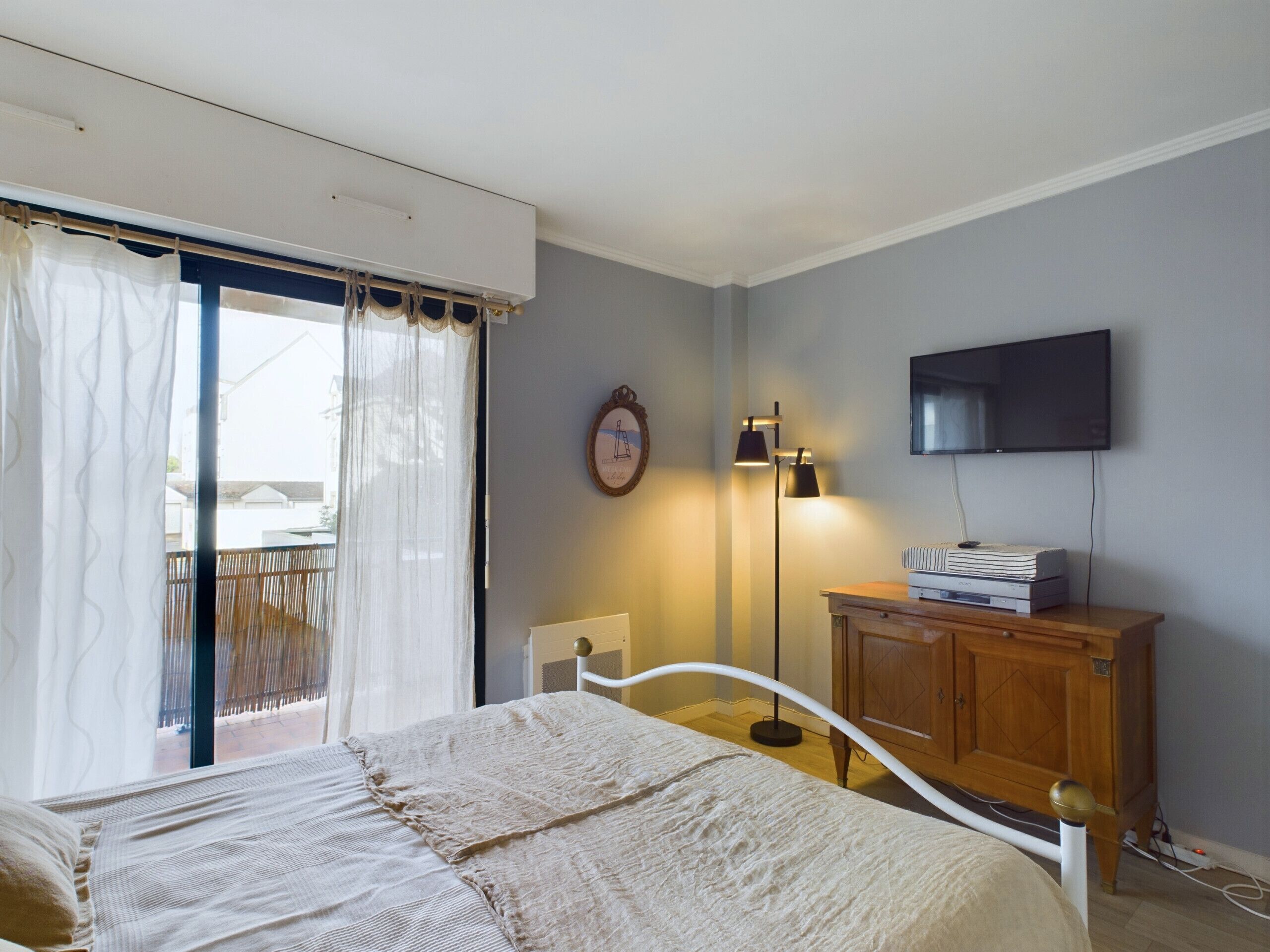 Un dormitori amb un llit, un televisor fixat a la paret, un armari de fusta i una làmpada de peu.