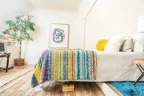 Une chambre à coucher avec un lit, une plante en pot, un tableau encadré et un téléviseur posé sur une table en bois.