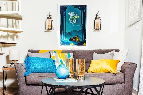 Un salon avec un canapé gris, des coussins colorés, un vase bleu et deux grands vases en verre posés sur une table basse.