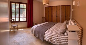 Ein Schlafzimmer mit Bett, Stuhl, Kleiderschrank und einem fenster mit Vorhängen.