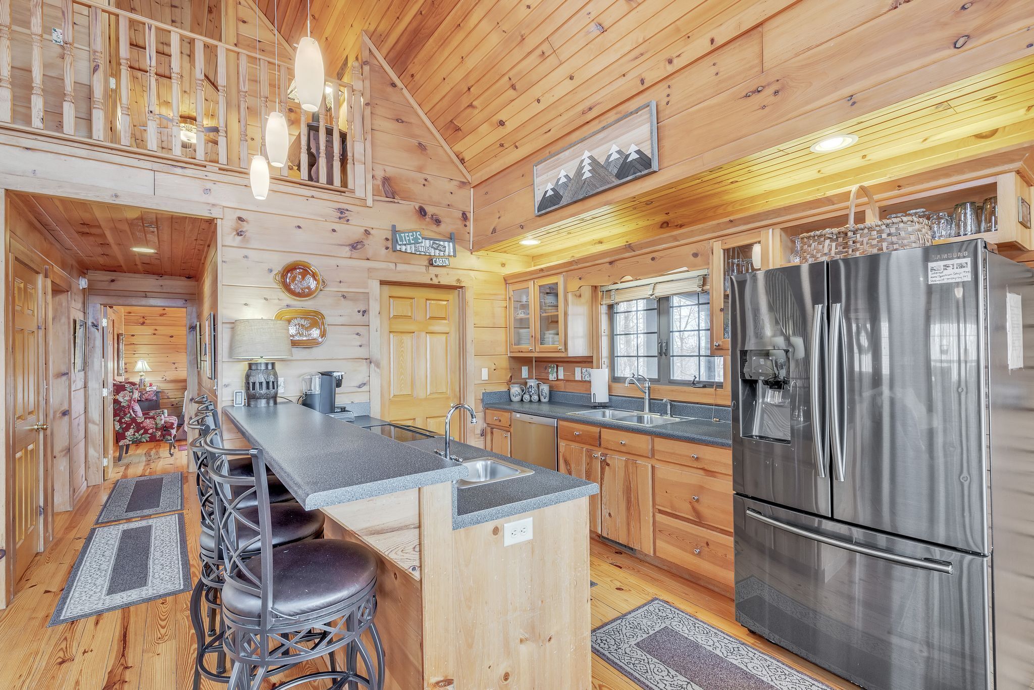 L’intérieur d’une cabane en bois comprend une cuisine équipée d’un réfrigérateur en acier inoxydable, de meubles en bois et d’un coin bar avec des tabourets.