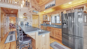 A wooden cabin interior with a kitchen featuring a stainless steel refrigerator, wooden cabinets, and a bar area with stools. - Experience Luxury at The Sanctuary in Hendersonville (Hendersonville)