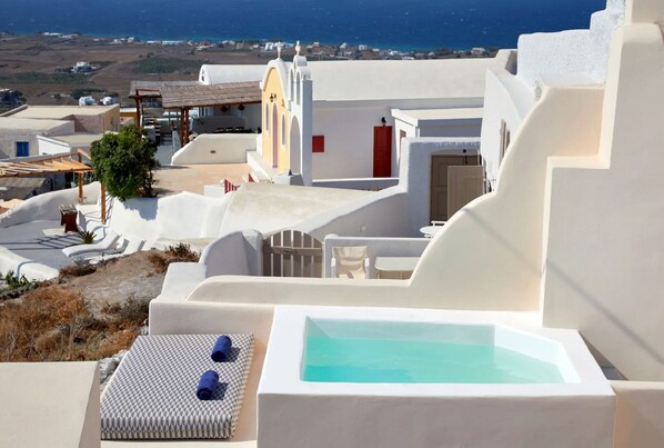 A white-walled building with a pool, outdoor seating, and a view of the sea.