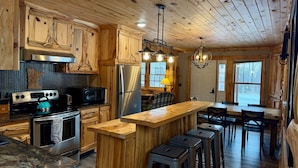 A rustic cabin-style kitchen with wooden cabinets, a stainless steel refrigerator, a gas stove, and a bar area with stools. - 8 Min to State Parks|Sauna|Fire Pit| (Beaver Bay)
