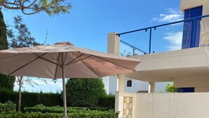 Una terraza con sillones, una mesa con bebidas y una sombrilla grande.