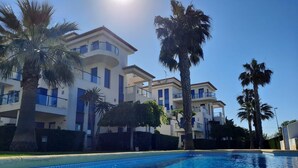 Un moderno edificio de varios pisos con balcones, piscina y palmeras.