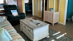 A living room with a green armchair, a striped sofa, a white chest of drawers, and a wicker cabinet.
