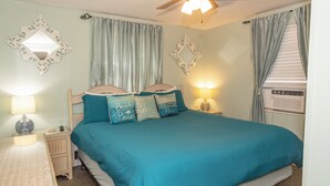 A bedroom with a bed, two bedside tables, a ceiling fan, and a window with curtains.