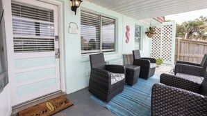 A covered porch with wicker furniture, a welcome sign, and a doormat.