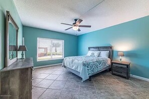 A bedroom with a bed, a ceiling fan, a nightstand, a dresser, and a window with blinds.