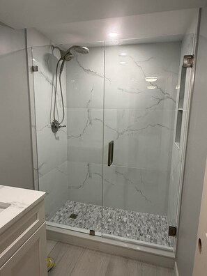 A glass-enclosed shower with a marble finish, a visible showerhead, and a small window at the bottom.
