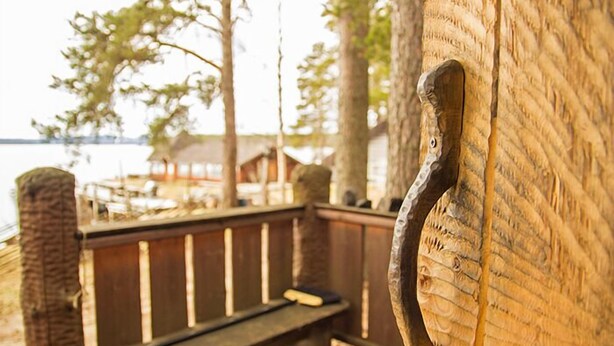 A wooden bench on a deck with a view of a body of water and trees in the background.