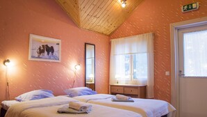 A hotel room with two beds, a window with curtains, a wooden ceiling, and a picture on the wall.