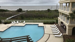 Une piscine avec des chaises longues, une vue sur l’océan et un bâtiment doté de balcons.